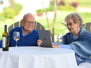 Couple in blue looking at an iPad, enjoying a glass of white wine