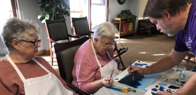 Two senior women paint with guidance from an instructor.