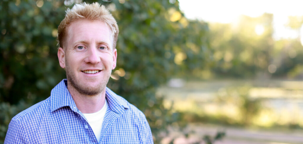 Matt, environmental services and maintenance director at Elim Shores Assisted Living, smiling outdoors with a scenic background of trees and water.