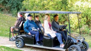 Elim Shores residents ride a golf cart through the wooded walking path, enjoying fresh air and connection.