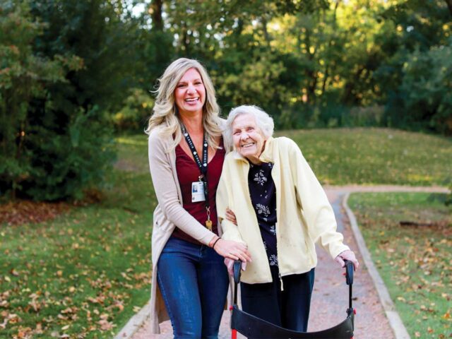 Elim Shores resident walking with a staff member on the lakeside path, enjoying fullness of life and scenic nature.